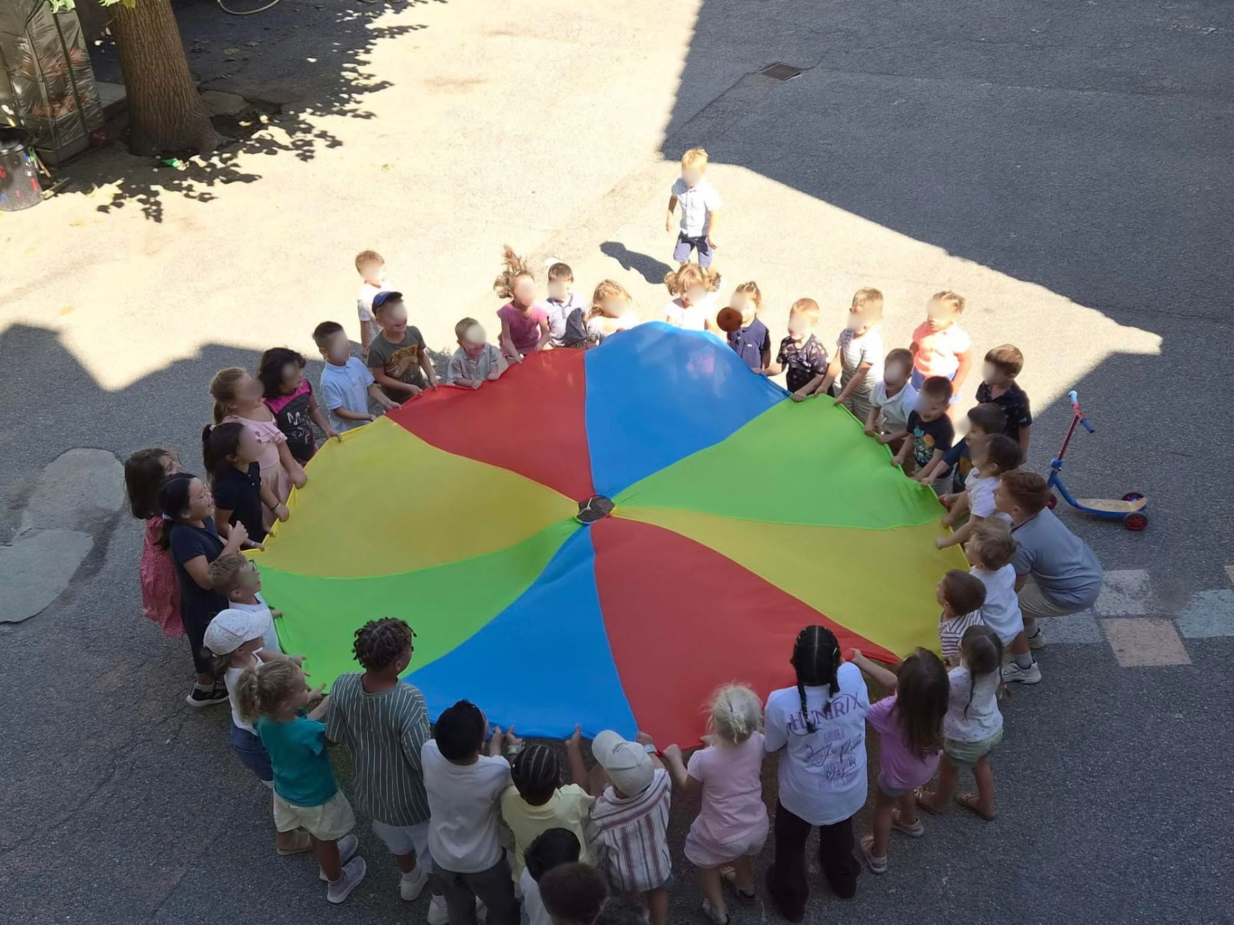 Les enfants réunis autour d'un parachute coloré dans la cour de l'école