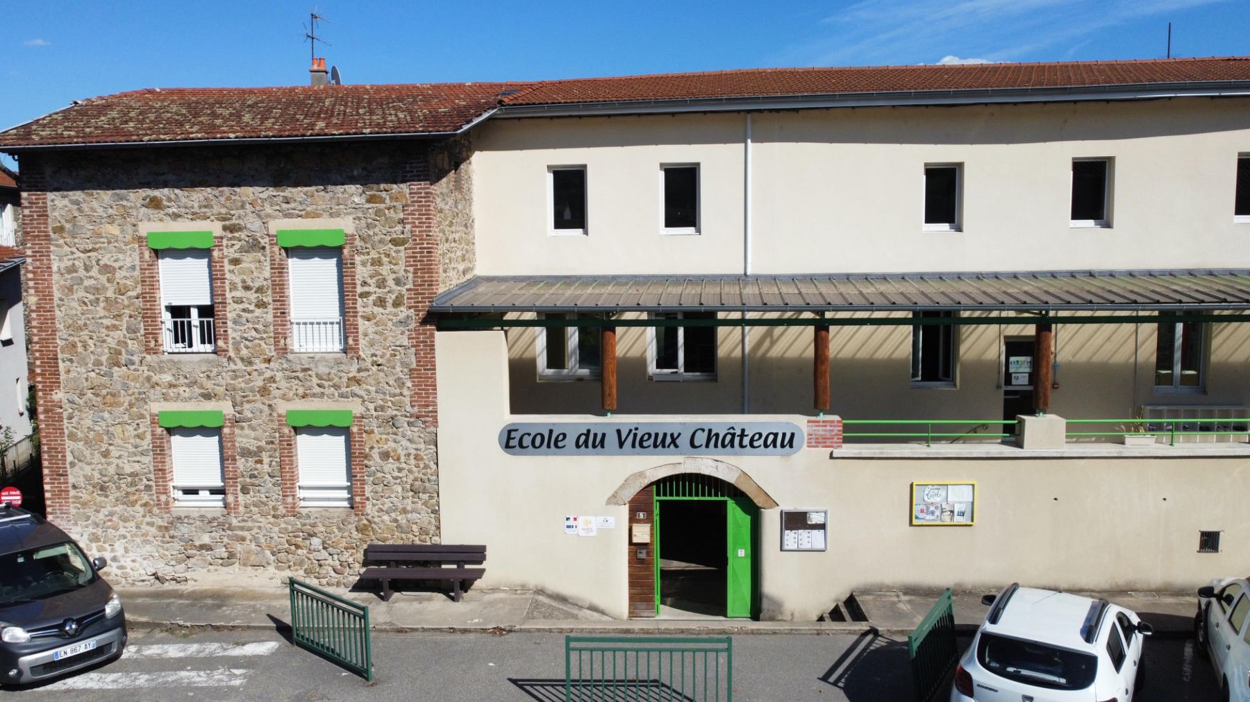 La façade en pierre de l'école et sa cour plantée d'arbres